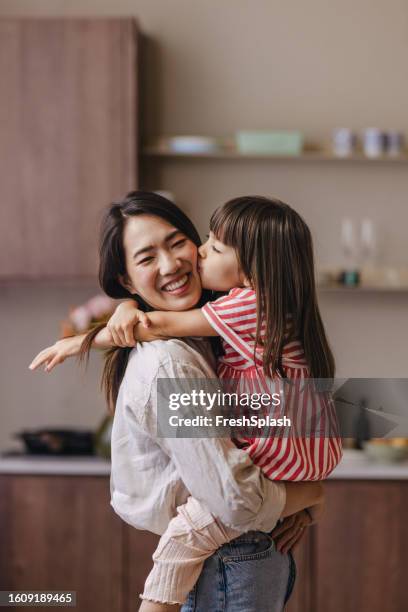 a happy cute asian girl hugging and kissing her mother - mother and daughter kissing stock pictures, royalty-free photos & images