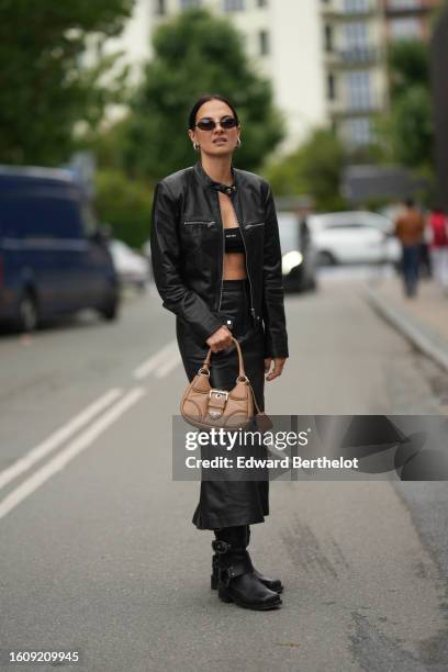 Guest wears black sunglasses, silver earrings, a black shiny leather zipper jacket, a black shoulder-off / cropped top from Miu Miu, a black shiny...