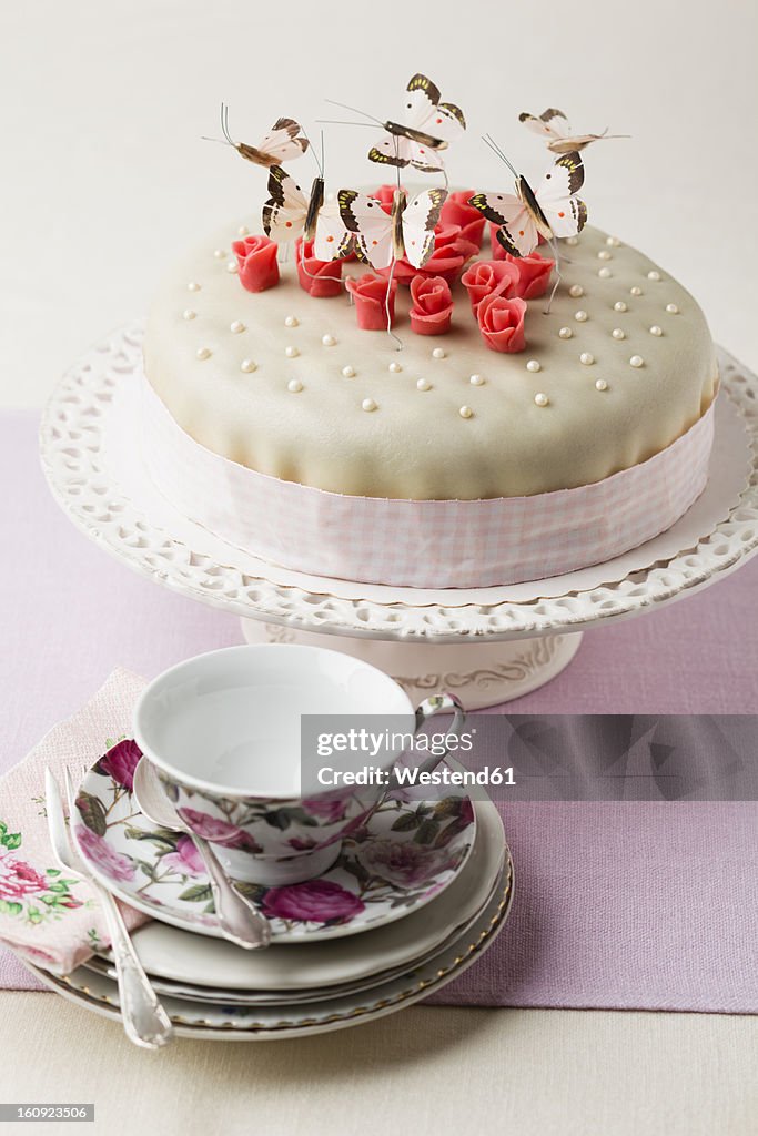 Cake decorated with butterflies shaped and marzipan, cup and saucer in foreground