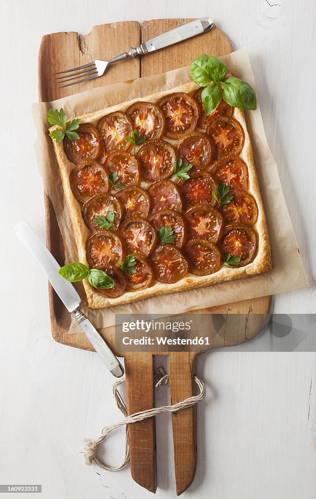 Puff pastry tarte garnished with tomato slices and herb on chopping board
