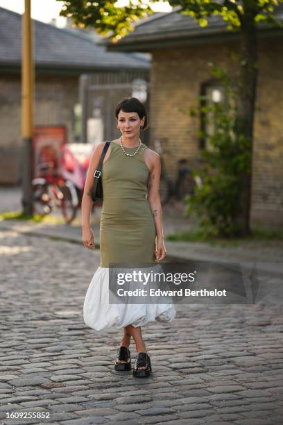 Guest wears silver earrings, a silver pearls necklace, a pale khaki halter-neck / long tube dress with white puffy large borders, a black shiny...