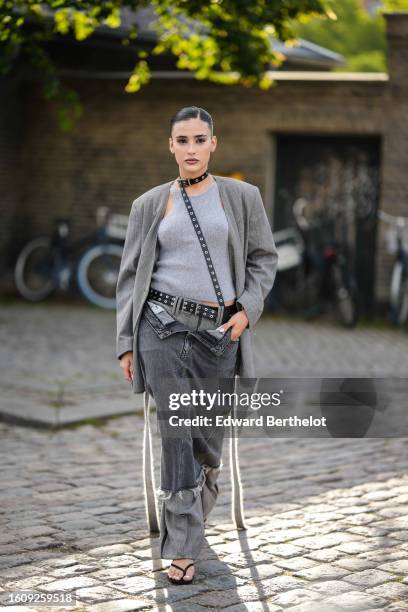 Guest wears a black shiny leather nailed / studded belt as a necklace, a pale gray halter neck tank-top, a pale gray blazer jacket, a black shiny...