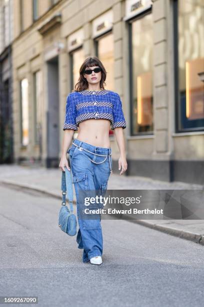 Guest wears black sunglasses, a blue denim and black and white houndstooth print pattern striped print pattern short sleeves / cropped t-shirt, a...