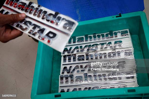 An employee takes a Mahindra & Mahindra Ltd. Navistar truck emblem badge out of a tray on the assembly line at the company's factory in Chakan,...