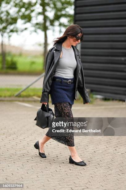 Guest wears black sunglasses, gold small earrings, a pale gray t-shirt, a black shiny leather zipper jacket, a black shiny leather belt, a navy blue...