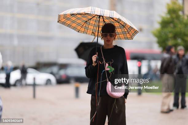 Katya Tolstova seen wearing Burberry umbrella, black and golden asymmetric sunnies, yellow see through earrings, distressed black sweater with...