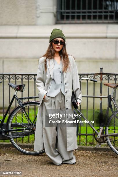 Guest wears a khaki wool beanie, black shiny sunglasses, a pale gray buttoned gilet, a pale gray long buttoned coat, pale gray oversized wide legs...