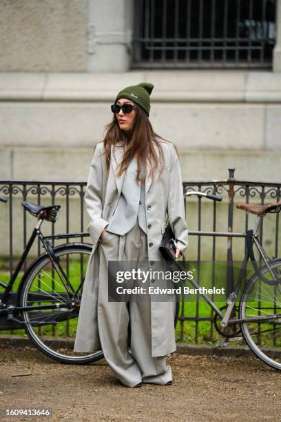 Guest wears a khaki wool beanie, black shiny sunglasses, a pale gray buttoned gilet, a pale gray long buttoned coat, pale gray oversized wide legs...