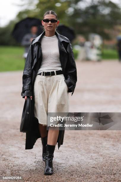 Sophia Geiss seen wearing black thin sunnies, silver hoop earrings, white crocheted top, long black leather coat, black belt with silver hardware,...