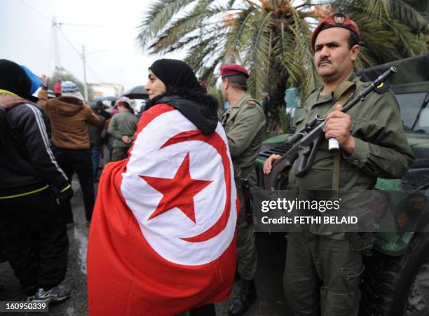 Woman wrapped in a national flag walks past a Tunisian soldier standing guard during late opposition leader Chokri Belaid's funeral procession which...