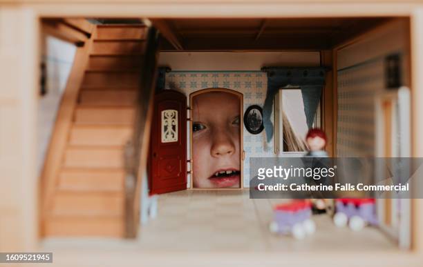 a little girl looks through the doorway of a dolls house filled with furniture and miniature dolls - miniature dollhouse bildbanksfoton och bilder