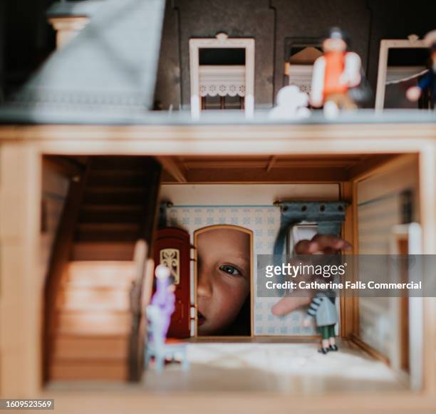 a little girl looks through the doorway of a dolls house filled with furniture and miniature dolls - skimpy girls stock pictures, royalty-free photos & images
