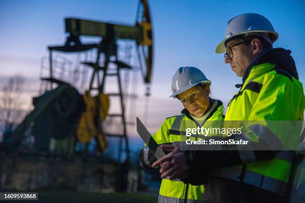 professionals planning over laptop while standing against oil pump during sunset - boormachine stockfoto's en -beelden