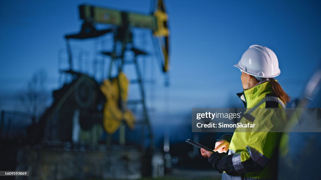 Ingénieur regardant des machines tout en utilisant une tablette PC à l’industrie pétrolière contre ciel