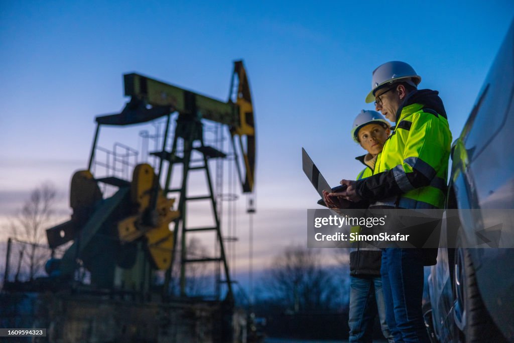 Partners planning over laptop while standing against equipment by car at field