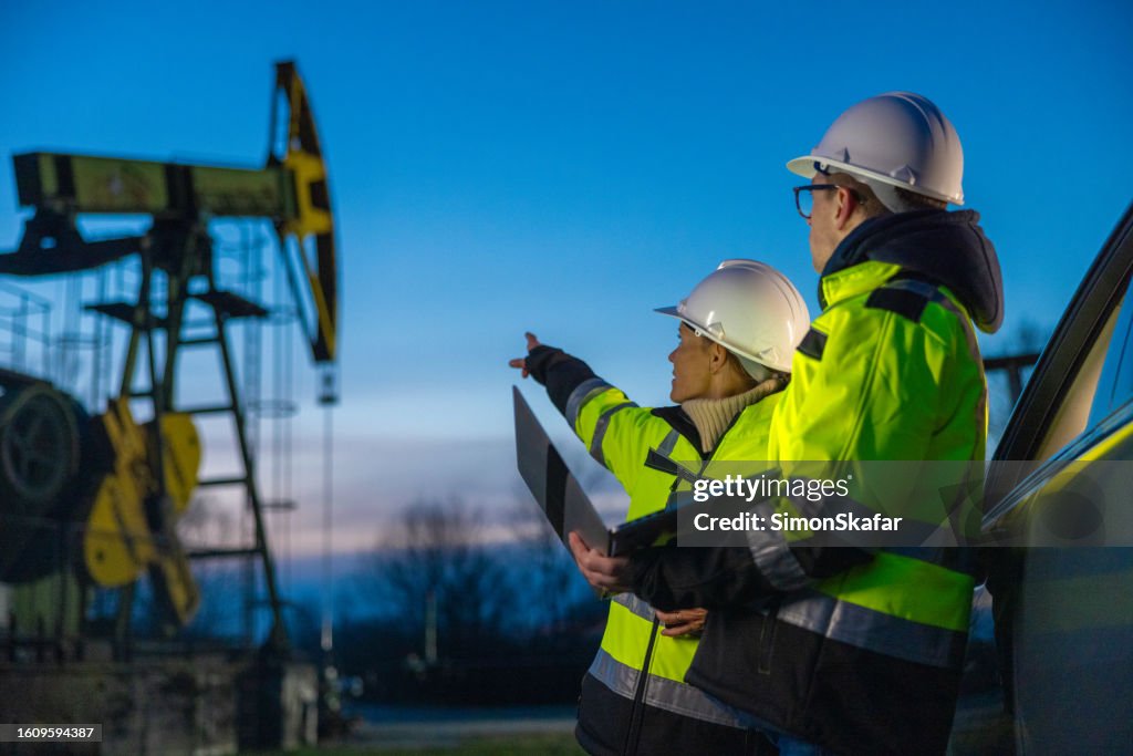 Des ingénieurs examinent des machines tout en planifiant sur un ordinateur portable en voiture dans un champ pétrolifère