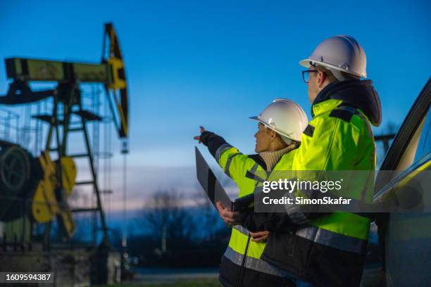 engineers looking at machinery while planning over laptop by car at oil field - plataforma petrolífera imagens e fotografias de stock