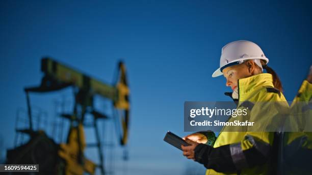 female worker using tablet pc while standing by car at oil field against sky - operário petrolífero imagens e fotografias de stock