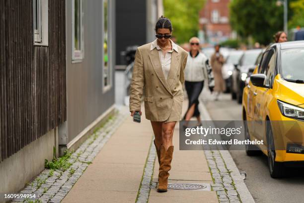 Guest wears black sunglasses, a gold necklace, a white latte shirt, a beige oversized blazer jacket as a dress, camel suede pointed / block heels...