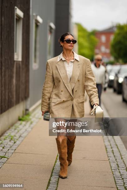 Guest wears black sunglasses, a gold necklace, a white latte shirt, a beige oversized blazer jacket as a dress, camel suede pointed / block heels...