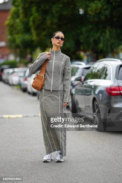 Guest wears black sunglasses, silver earrings, a pale gray with embroidered white striped print pattern high neck zipper sweater, a matching pale...