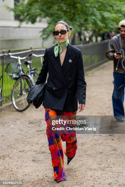 Guest wears black blazer, scarf, red orange printed beige pants outside Mark Kenly Domino Tan during the Copenhagen Fashion Week Spring/Summer 2024...