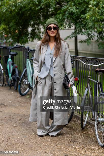 Guest wears green beanie, grey oversized coat, pants, vest outside Mark Kenly Domino Tan during the Copenhagen Fashion Week Spring/Summer 2024 on...