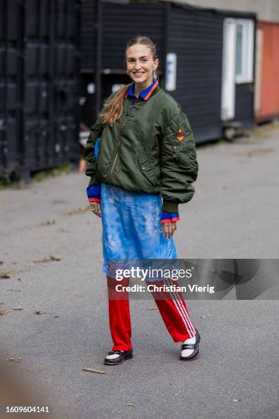 Guest wears green bomber jacket, red Adidas track suit pants, blue dress outside Helmstedt during the Copenhagen Fashion Week Spring/Summer 2024 on...