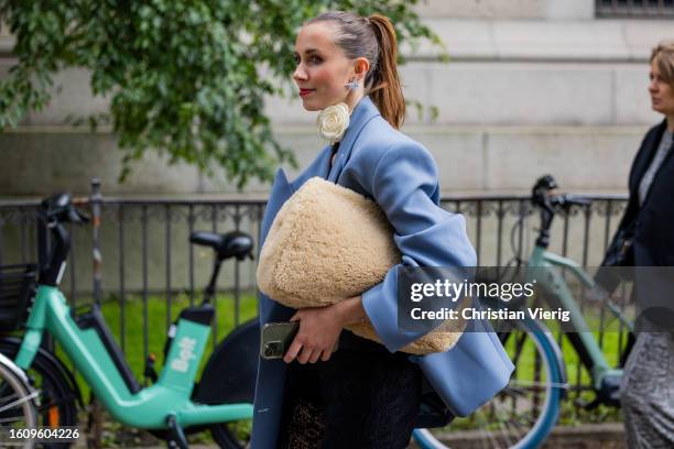 Guest wears beige teddy bag, blue oversized blazer outside Mark Kenly Domino Tan during the Copenhagen Fashion Week Spring/Summer 2024 on August 10,...