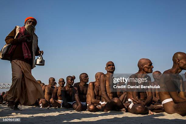 Naga sadhus, naked Hindu holy men, wait for food during their initiation ceremony on the banks of the Ganges river during the Maha Kumbh Mela on...