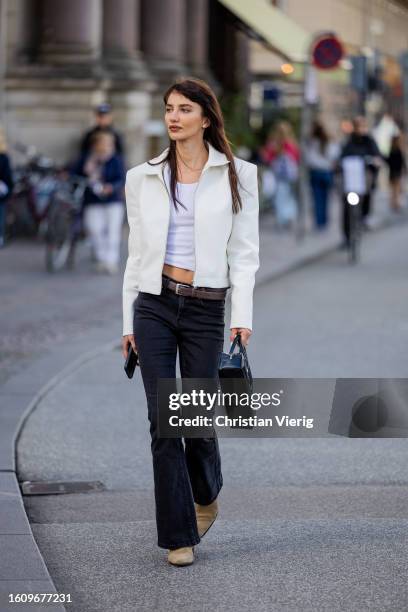 Guest wears white blazer, black long bag, black denim jeans, brown boots outside Rotate during the Copenhagen Fashion Week Spring/Summer 2024 on...