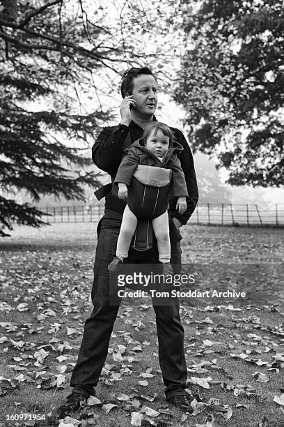 British Prime Minister David Cameron pauses to take a phone call from his Downing Street office during a Saturday morning walk with baby daughter...