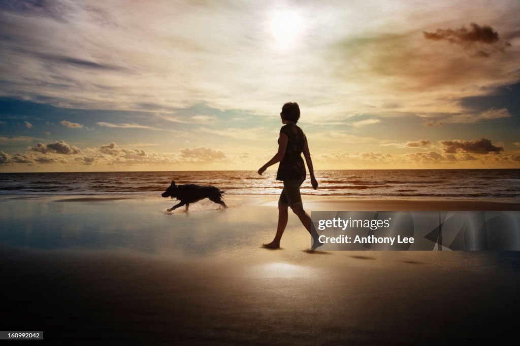 Silhouette of woman and dog walking on beach