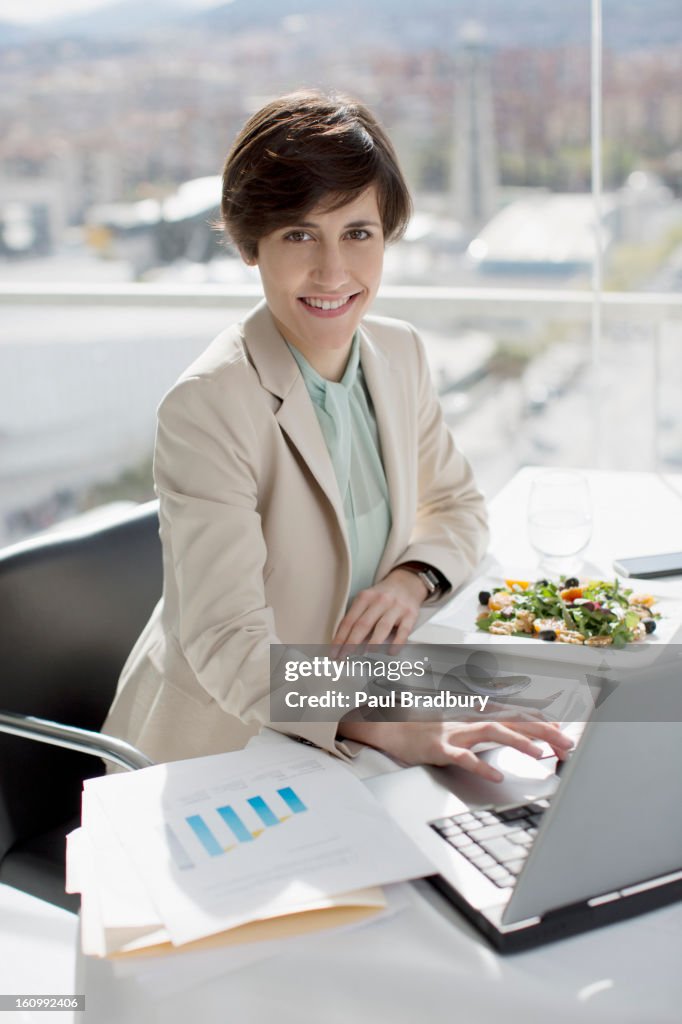 Porträt von lächelnd Geschäftsfrau Essen Mittagessen und Arbeiten am Schreibtisch