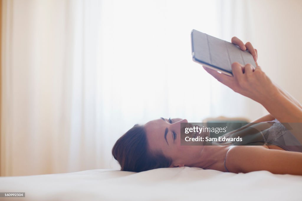 Smiling woman laying on bed and using digital tablet