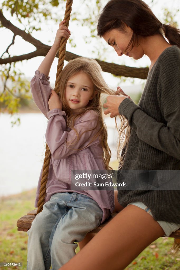 Mother braiding daughterês hair on swing at lakeside