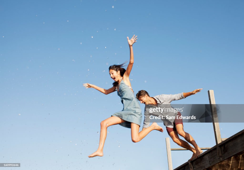 Exuberant couple jumping off dock