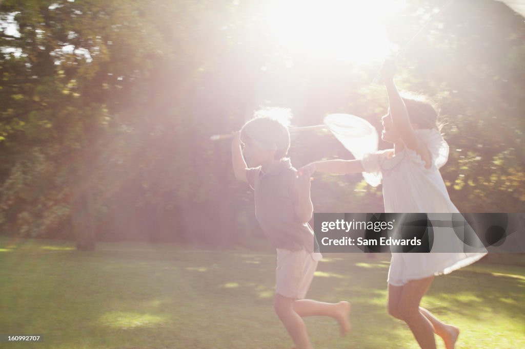 Boy and girl holding hands and running with butterfly nets in grass