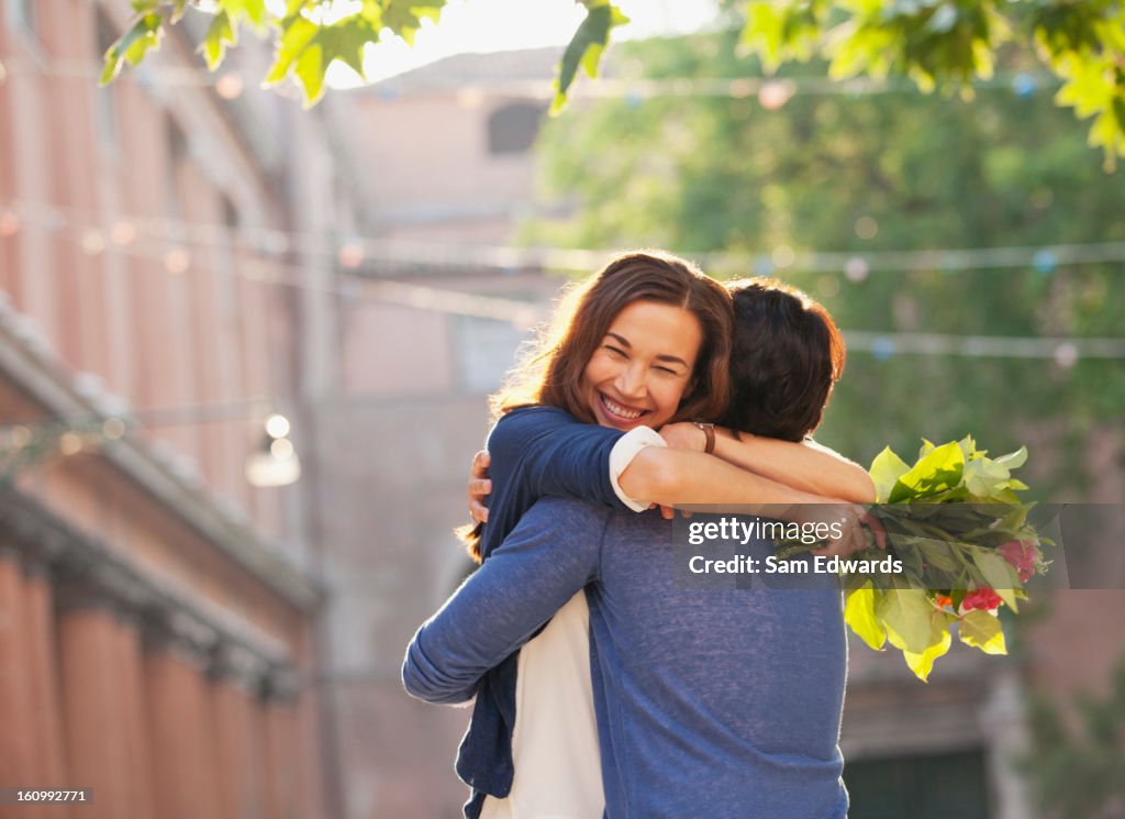 Smiling woman with flowers hugging man