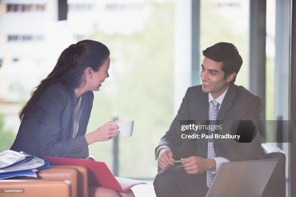 "Smiling businessman and businesswoman with coffee, laptop and paperwork"