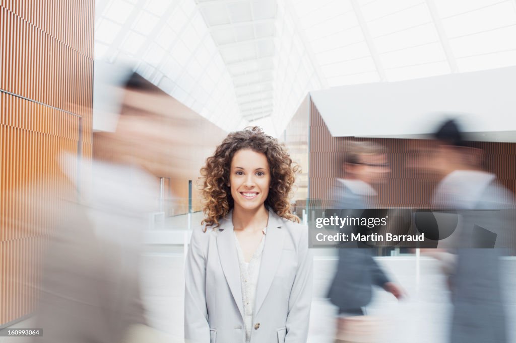 Portrait of serious woman with co-workers rushing by in lobby