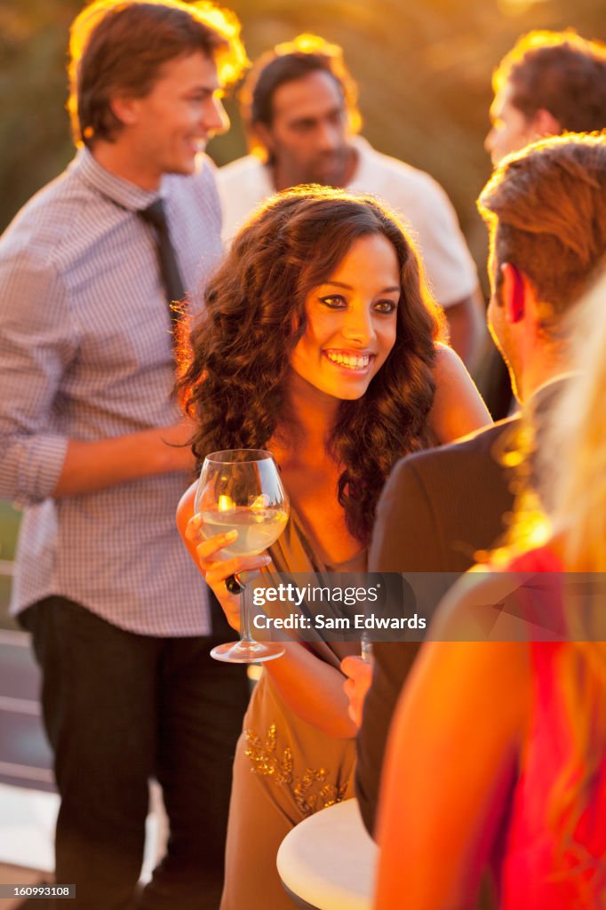 Smiling woman with wine glass talking to man on sunny balcony