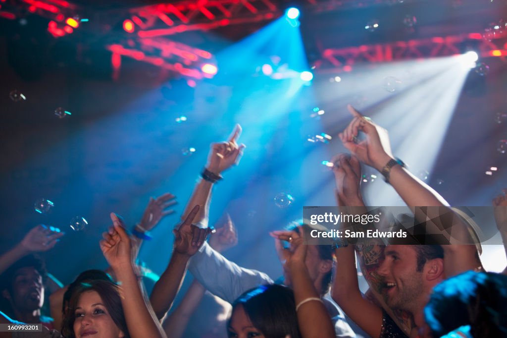 Enthusiastic crowd with arms raised on dance floor of nightclub