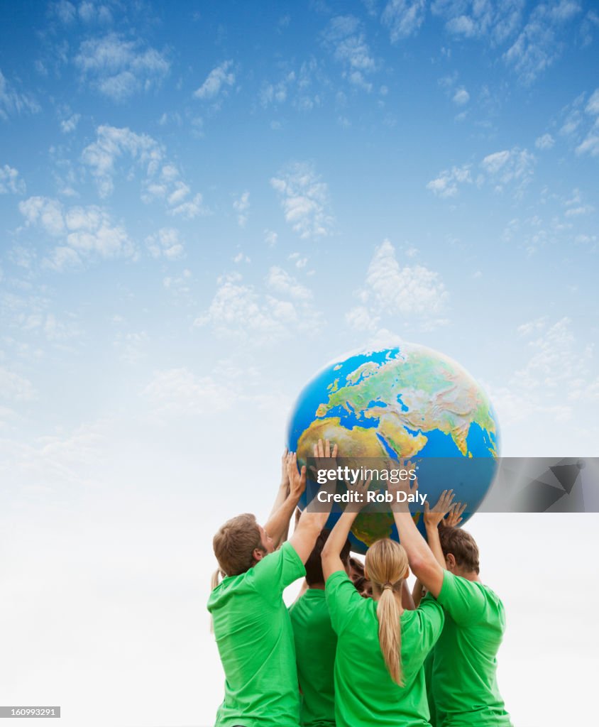 Team in green t-shirts lifting globe overhead