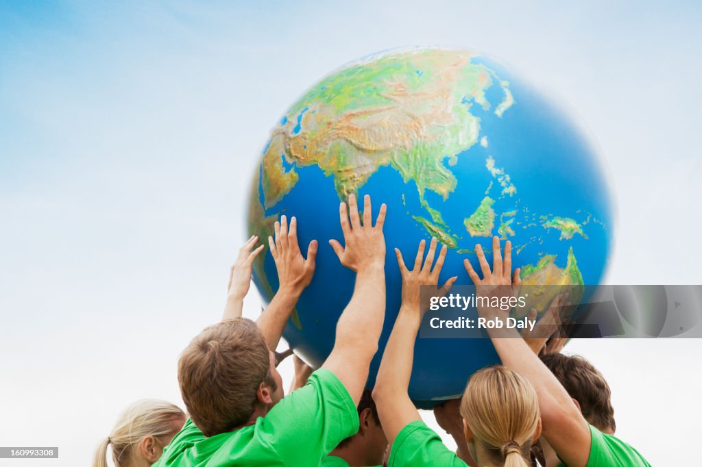 Team in green t-shirts lifting globe overhead