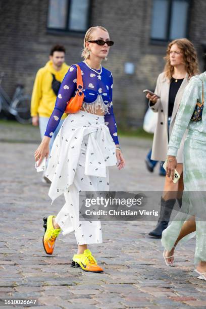 Guest wears white skirt with print, orange bag, Nike shoes, top with heart print outside Ganni during the Copenhagen Fashion Week Spring/Summer 2024...