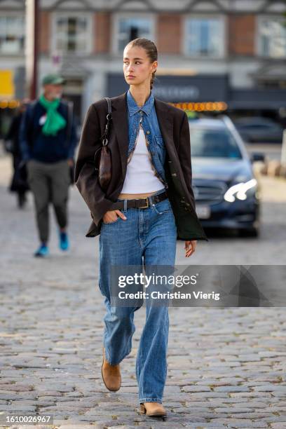 Guest wears denim jeans, shirt, brown oversized blazer outside Ganni during the Copenhagen Fashion Week Spring/Summer 2024 on August 10, 2023 in...