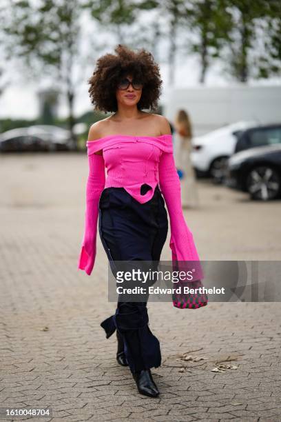 Guest wears black sunglasses, a neon pink shoulder-off / long flared sleeves ribbed wool top, a navy blue striped print pattern long skirt, a neon...