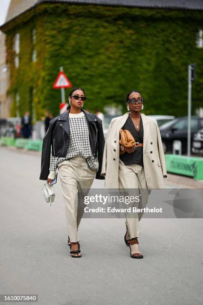 Guest wears black sunglasses, silver earrings, a beige with black checkered print pattern pullover, a black shiny leather zipper jacket, beige suit...