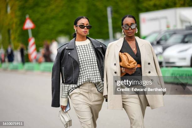 Guest wears black sunglasses, silver earrings, a beige with black checkered print pattern pullover, a black shiny leather zipper jacket, beige suit...